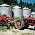 Man sitting beside red tractor and combine.