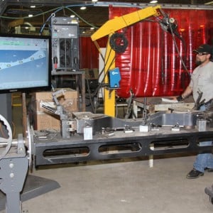 Senior welder Ted Nelson supervises a robotic process that will finish-weld a front tractor axle held in this jig.