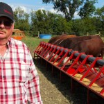 “A few years ago Dennis McMorris got tired of packing buckets of grain to feed his 350 head of cattle on his farm near Balcarres, Sask. Seaching for “that better way” he eventually developed the Bovine Bucket feeding system which has gone through extensive research and development improvements over the years. The system includes an overhead hopper on one end of the feed auger. The computerized control panel can be set so the auger delivers and drops a measured among of grain out along the feed trough on whatever timing schedule the producer wants. The unit comes in whatever length needed for any size herd. McMorris says he set up the system on his farm so he could feed four different groups of cattle with one Bovine Bucket system — feed grain or ration to a herd of pregnant cows, for example, move them out, then open a gate and bring in a group of weaned calves and so on. The Bovine Bucket was one of the exhibitors at the first-ever Ag In Motion farm show this week near Saskatoon. Along with the Bovine Bucket there were other displays of livestock handling and management equipment. The livestock component of the outdoor farm show will be expanding in future years. For more information on the Bovine Bucket visit their website at: www.bovinebucket.ca.