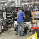 Employees ready the engine and transmission for installation. 