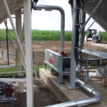 The system consists of an air lock under the bin or a meter where the grain flows through into the airstream and then a blower that pneumatically moves the air to the bins. A moveable distributor at ground level channels the grain to different bins. The initial cost of this pneumatic grain-handling system was $60,000, but the Neufelds believe it has been worthwhile. (see more photos below)