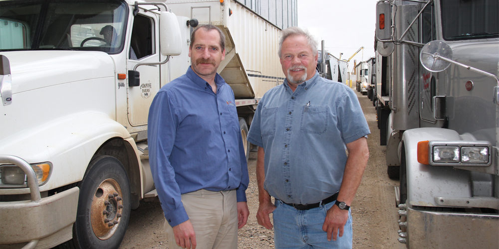 Jason Labossiere, left and Curt Larsen between trucks delivering grains, oilseed and pulse crops to the Northgate terminal in southern Saskatchewan.