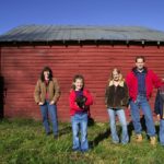 Family portrait standing in front of a red barn on the farm.