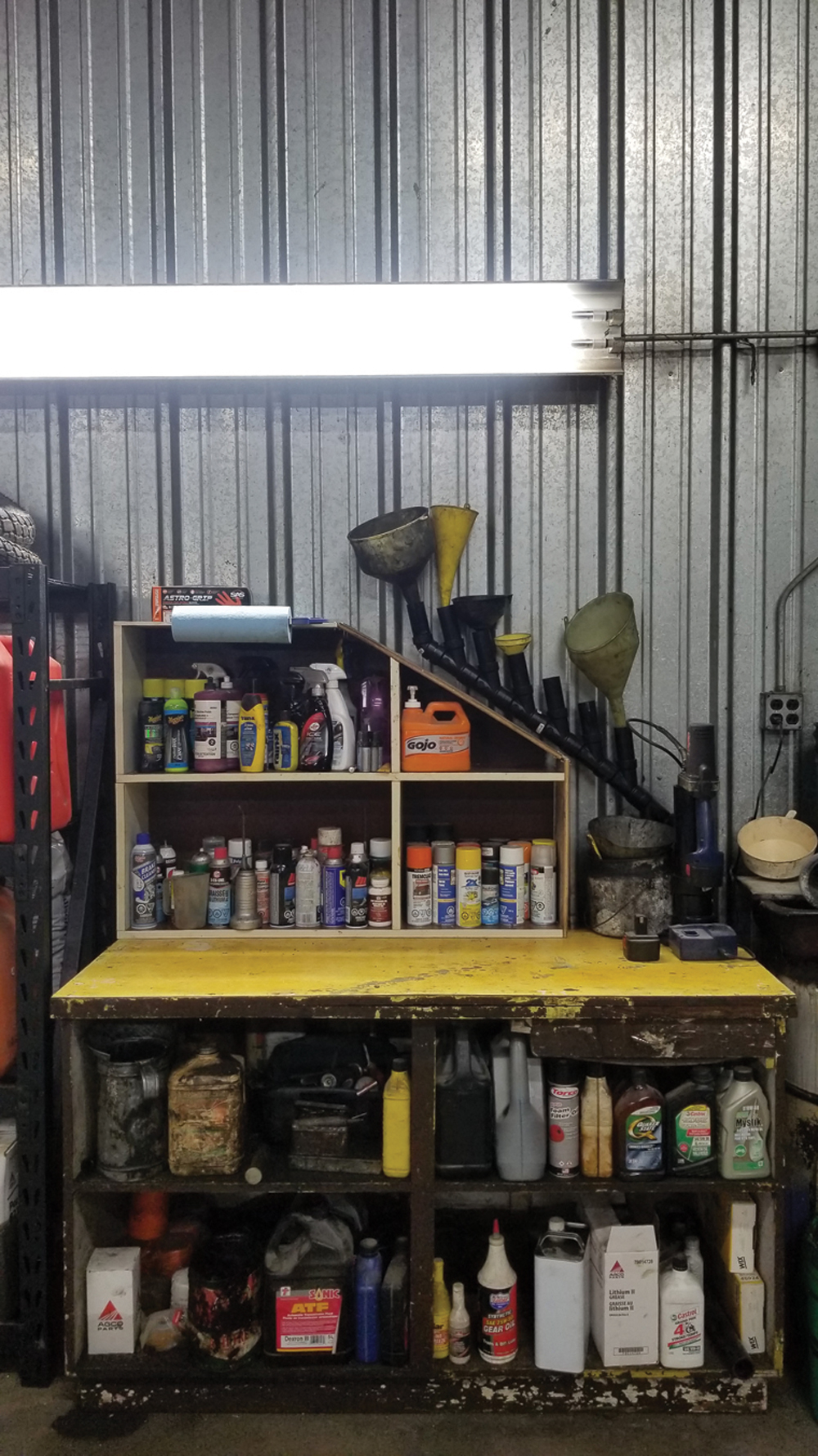 Previously, this was our grease table/lubrication shelf. I built a funnel rack (each funnel drains into a container at the bottom of the pipe) and a grease-gun holder out of ABS pipe, augmented an old shelving unit to fit under the rack for aerosols and mounted a towel dispenser to it. 