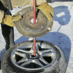 A steel plate set on top of a car tire and rim will hold the spool of barbed wire.