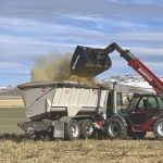 Dry alfalfa and straw bales are loaded into the Kuhn Side Slinger manure spreader, which doubles as a mixer wagon. The hay and straw will serve as biomass for the compost.