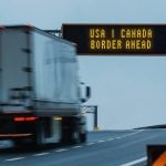 Semi truck approaching a border ahead highway sign. Composite image.