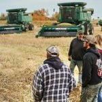 Group of people standing outside on farm field in Canada with agricultural machinery in background during harvest season. Pic: AJ_Watt/E+/Getty Images