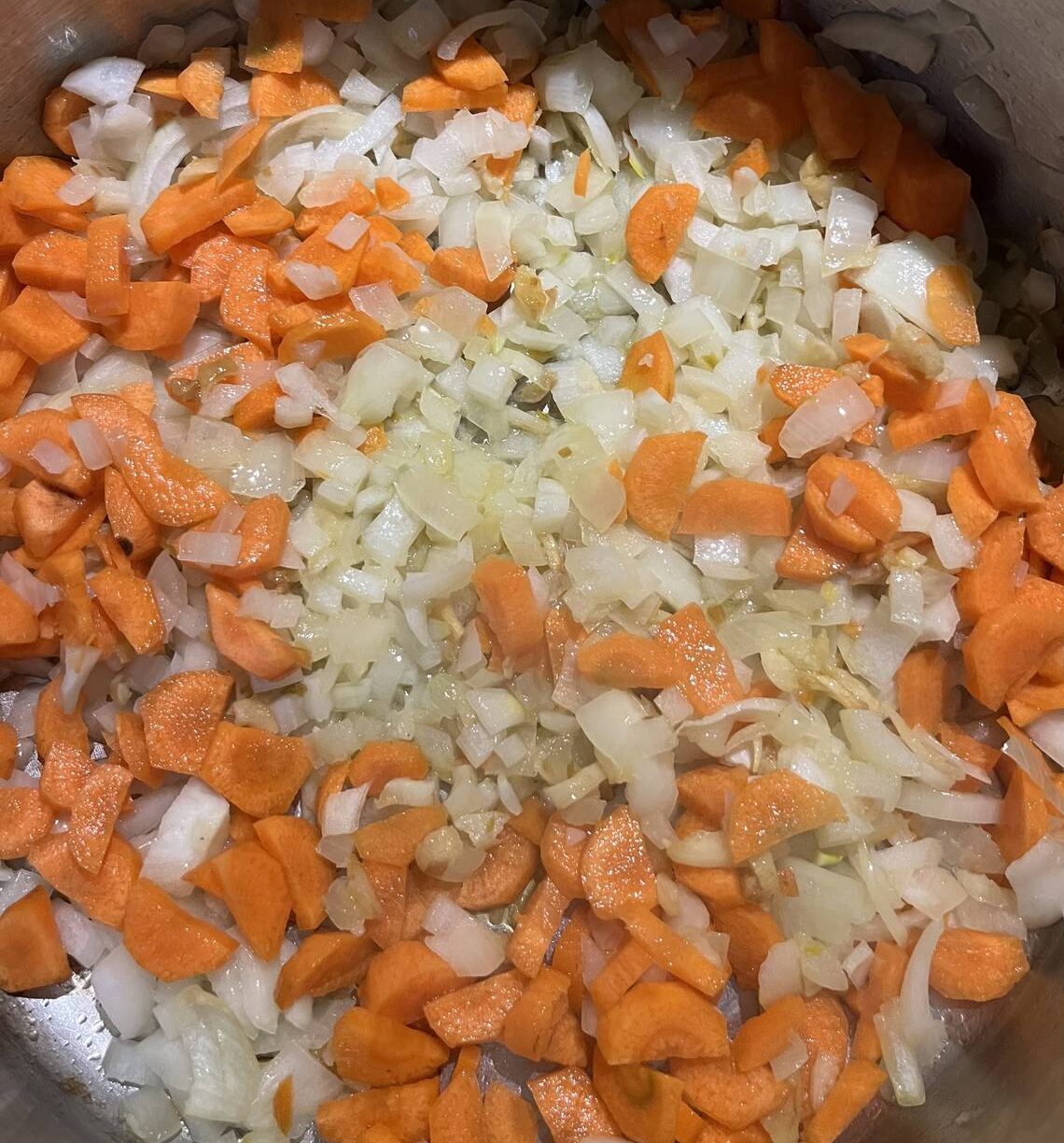 Base ingredients of onions and garlic with carrots for simple but nourishing potato and carrot soup as they start to sauté on the stove.
