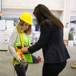 Woman in industrial workplace being fitted with personal protective equipment including bright yellow hard hat and safety vest. Photo: BulentBARIS/iStock/Getty Images