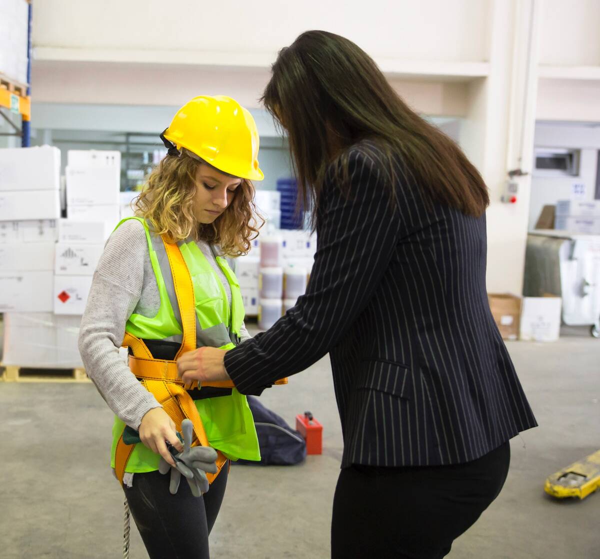 Woman in industrial workplace being fitted with personal protective equipment including bright yellow hard hat and safety vest. Photo: BulentBARIS/iStock/Getty Images