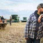 Mid adult man standing outside by his pickup truck on farm field with farmers taking break during harvest time