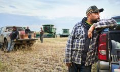 Mid adult man standing outside by his pickup truck on farm field with farmers taking break during harvest time