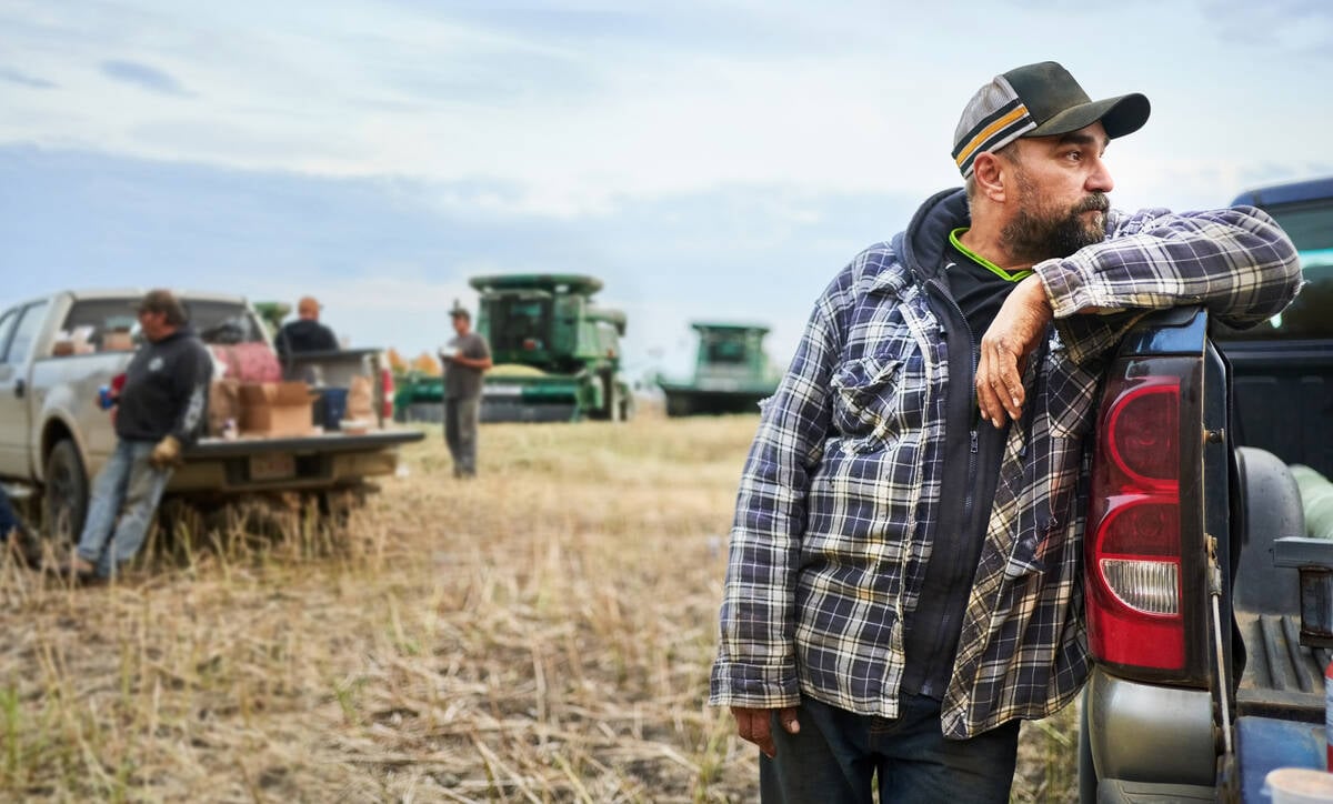 Mid adult man standing outside by his pickup truck on farm field with farmers taking break during harvest time