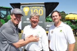 Jon Kennedy, left, president of Glacier Farm Media pins a 100-bushel canola button on Rob Saik of Agri-Trend Agrology, as Glen Walsh of John Deere looks on.